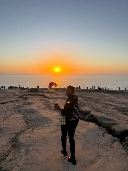 Maimuna Diallo on a rocky coastline at sunset